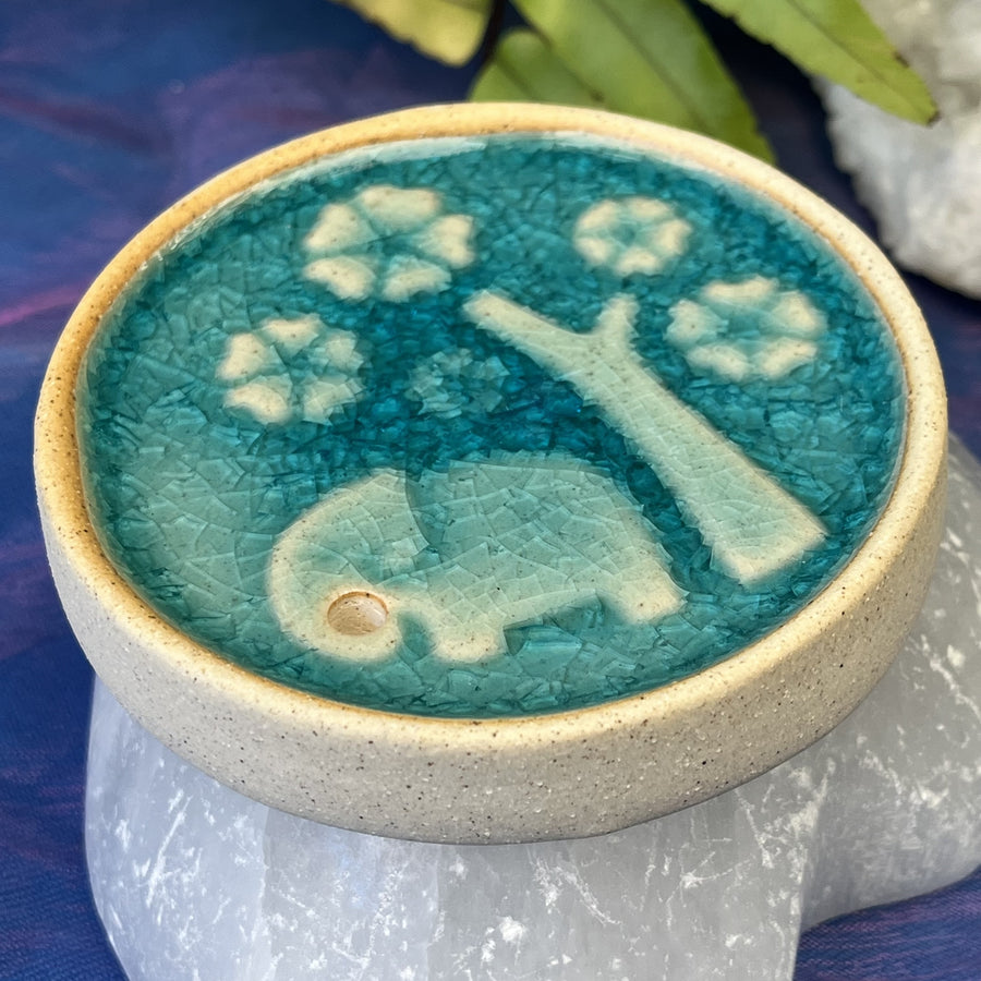 Himalayan Elephant – Round Incense Holder
A peaceful scene in miniature.

This 8.6 x 1.3 cm Japanese-style ceramic holder features a sweet elephant beneath blooming trees, glazed in rich Himalayan turquoise tones. Its round form evokes wholeness and grounding, while the imagery brings a gentle smile to your sacred space.

Perfect for stick incense—practical, poetic, and full of charm.

Let your incense rise from the heart of a quiet forest.